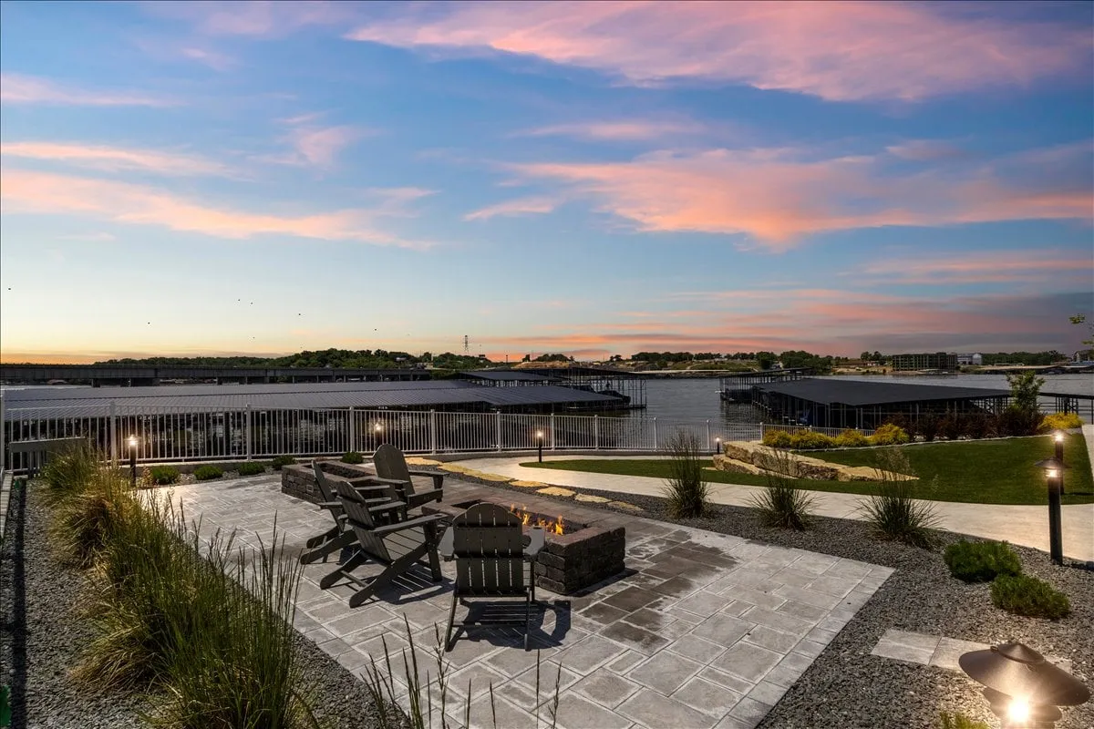 A cozy evening exterior shot of a fire pit surrounded by Adirondack chairs, with a waterfront view in the background. The setting invites stargazing, making s'mores, and intimate gatherings as the sun sets over the water.