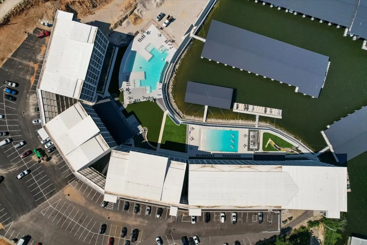 A vibrant exterior scene featuring a sparkling swimming pool, modern resort architecture, a marina with boats, and landscaped areas for relaxing or gathering. The lively atmosphere suggests both relaxation and social recreation, with water access visible just beyond the pool area.