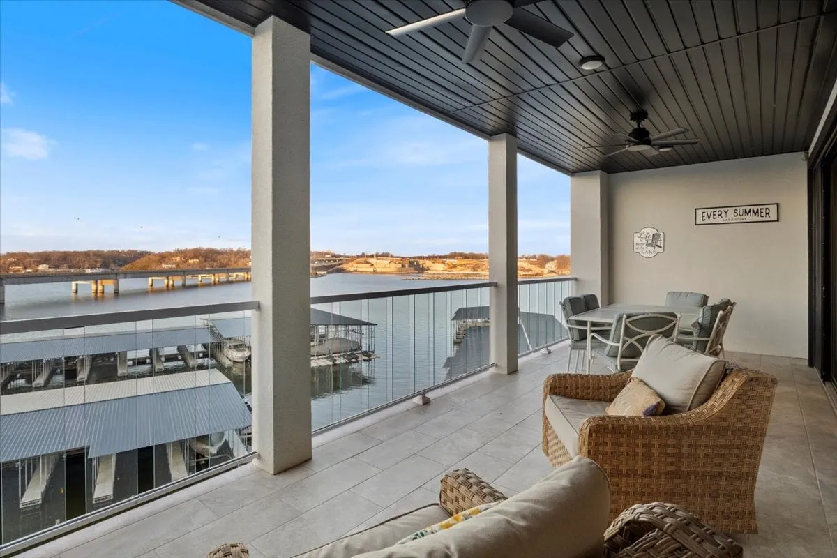 A tranquil waterfront balcony scene with comfortable outdoor seating and a decorative sign that reads 'EVERY SUMMER.' The view overlooks the lake, inviting moments of relaxation, sunrise breakfasts, or stargazing at night.