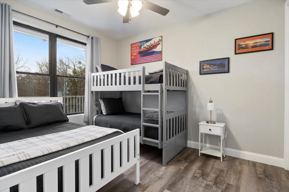 A family-friendly secondary bedroom with a bunk bed and a twin bed. The window lets in natural light, while decorative wall art and a nightstand with a lamp create a playful yet restful atmosphere, ideal for children or friends sharing a room.