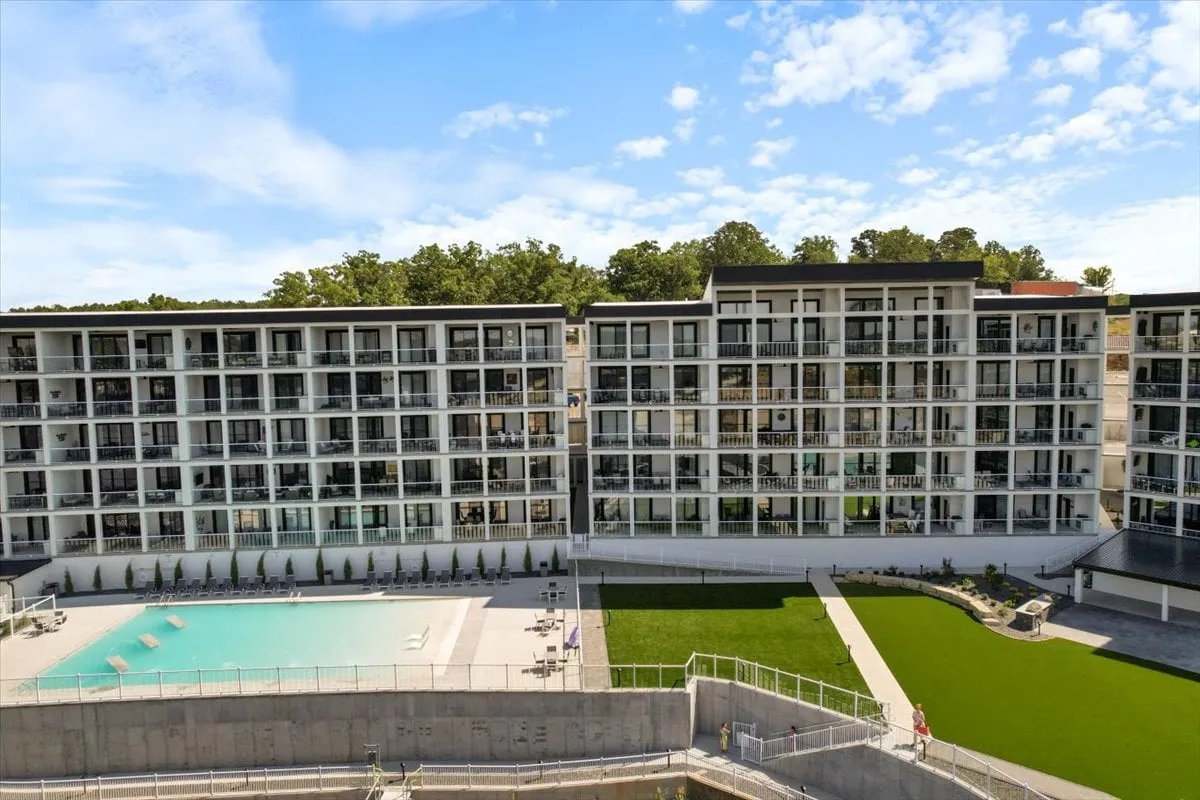 An inviting exterior scene featuring a beautiful swimming pool, green lawn, and condo balconies—some with sunset views. Friends and couples can be imagined enjoying poolside relaxation, socializing, or soaking in the calming atmosphere.
