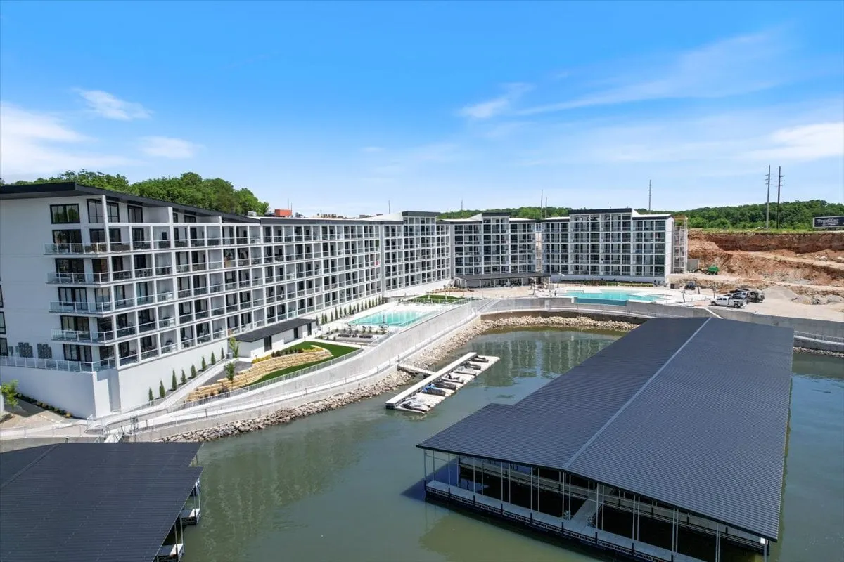 The modern building structure of Lake Loft is complemented by a large swimming pool, marina, and landscaped gardens. The image captures guests enjoying boating, relaxing by the pool, and experiencing the vibrant lakeside lifestyle.