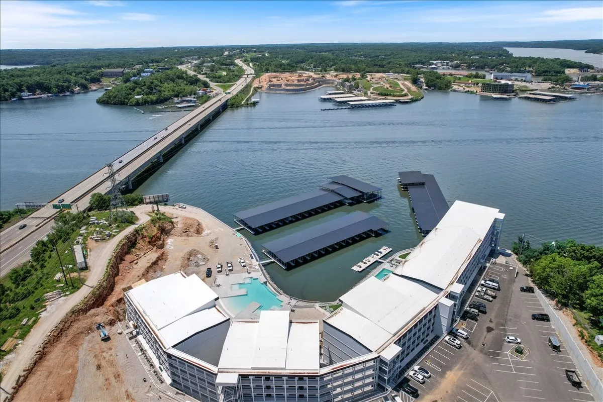 A panoramic exterior view showcasing the waterfront, marina, bridge, and lush landscape. The image captures boats docked along the shoreline, inviting guests to imagine boating and fishing adventures. The scene is bright and brimming with the energy of outdoor activities, set against the backdrop of the Lake of the Ozarks.